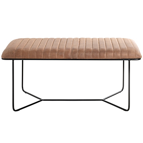 Un long banc avec une assise rembourrée beige. Le cadre en métal noir est en forme de croix.