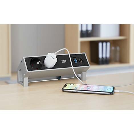 Multiprise grise avec prise et ports USB. Un chargeur est branché dans la prise, un smartphone est connecté.