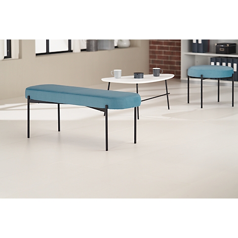 Blauw gestoffeerde bank met zwarte metalen poten, naast een witte tafel en krukken.