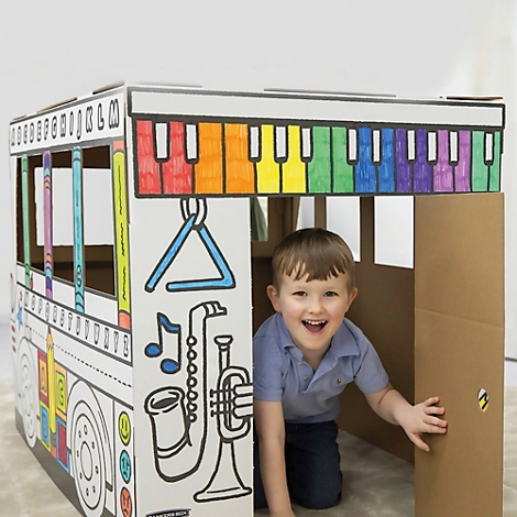 Un garçon souriant à l'intérieur d'un bus de jeu en carton peint. Un clavier coloré est représenté sur le toit. Des instruments de musique sont visibles sur le côté.