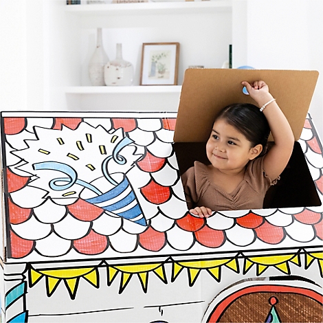 Une petite fille souriante regarde à l'extérieur d'une maison en carton faite maison. La maison est décorée de dessins colorés. Cela semble joyeux.