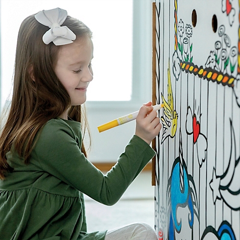 Une petite fille souriante colore un papillon sur un mur à colorier avec un marqueur jaune.