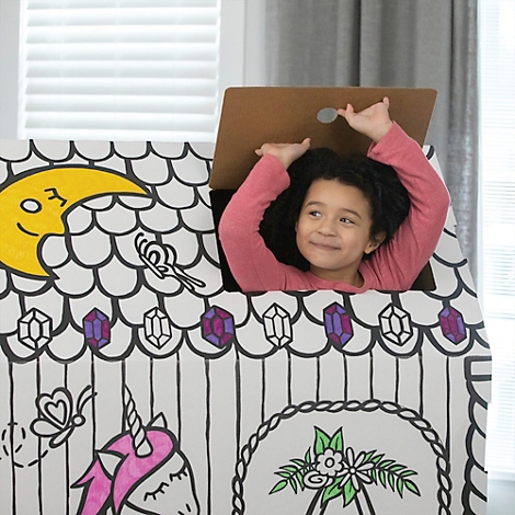 Un enfant souriant regarde à l'extérieur d'une maison en carton décorée de dessins de licornes et de lunes. L'enfant lève les bras.