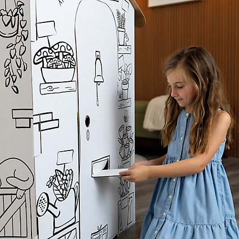 Een meisje met lang haar opent een brievenbus op een wit speelhuisje versierd met zwart omlijnde illustraties.