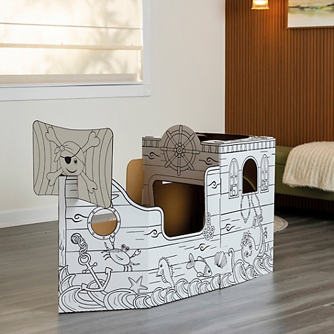 Une cabane de jeu en forme de bateau pirate en carton avec une voile de pirate, une ancre, des poissons et des vagues en guise de décoration. Il se trouve dans une pièce.