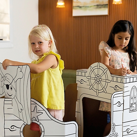 Twee meisjes spelen in een kartonnen schip, een met een ooglapje en een ster, de andere aan het roer.