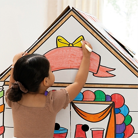 Een kind kleurt een kartonnen huis met een pen. Er staat een strik en een rode banner op het huis.