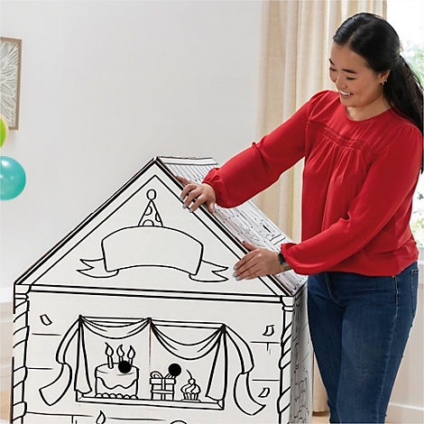 Een vrouw zet een kartonnen huis in elkaar met een verjaardagstaart en cadeaus erop.