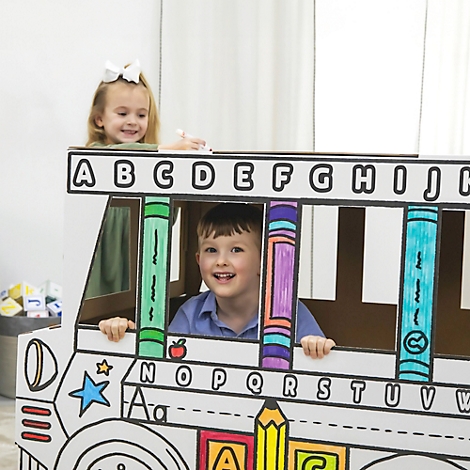 Zwei Kinder in einem bemalten Bus aus Pappe. Das Mädchen oben trägt eine Schleife, der Junge lächelt.