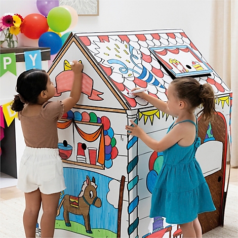 Zwei Mädchen malen ein Spielhaus mit Filzstiften an. Das Haus ist weiß mit bunten Dachziegeln und Dekorationen.