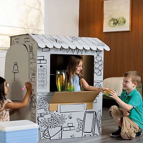 Trois enfants jouent avec une maison en carton peinte. Une fille tend une boisson à un garçon, tandis qu'un autre enfant peint.