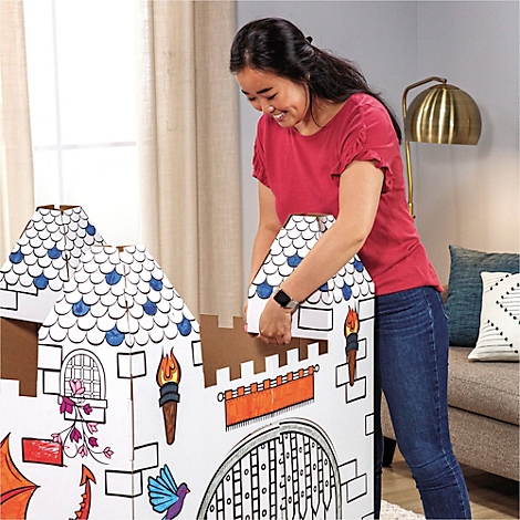 Une femme construit un château en carton, en ajoutant un toit. Le château est décoré de dessins colorés.