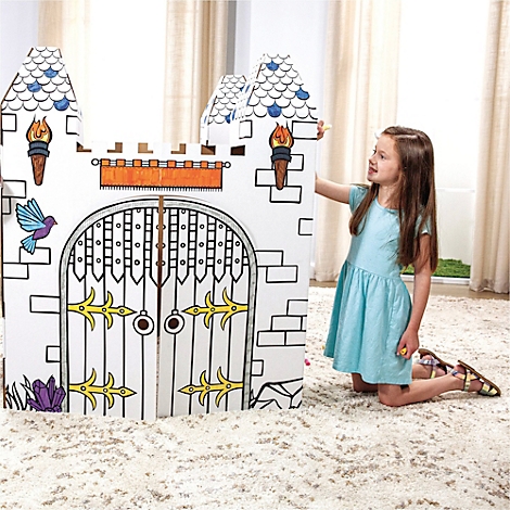 Fille agenouillée à côté d'un château en carton à peindre. Château avec créneaux, porte et tours. Jeune femme porte une robe bleu clair.