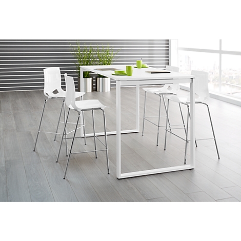 White table with bar stools, green decoration and windows in the background.