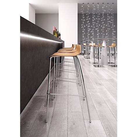 Row of bar stools in front of a bar; light wooden seats, metal legs, dark bar top, light wall.