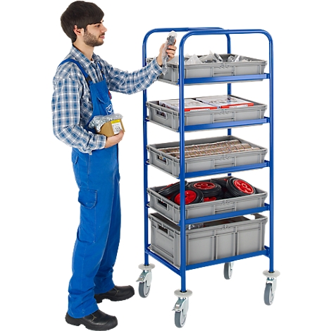 A man in blue overalls reaching into a box on a blue trolley. Grey plastic crates with tools and spare parts.