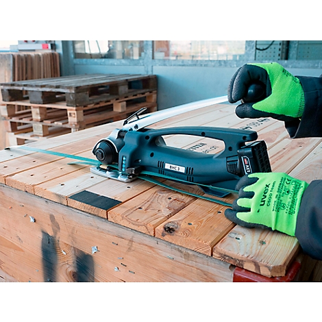 Persoon snijdt hout met een elektrische zaag. Handen met groene handschoenen houden de zaag en het hout vast.