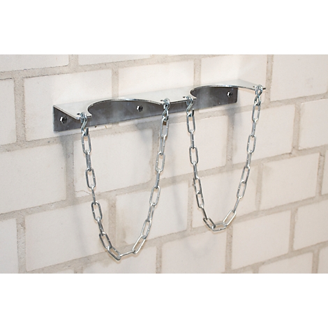 Metalen beugel met kettingen aan witte bakstenen muur. Houdt waarschijnlijk twee gasflessen.