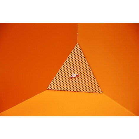 Ein orangefarbener Eckbereich mit einem perforierten dreieckigen Element, das an einer Wand befestigt ist, durch das ein kleiner Knopf verläuft.