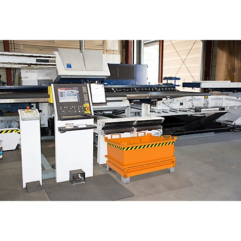 Industrielle Maschine mit Bildschirm und Bedienelementen. Orangefarbener Behälter mit schwarz-gelben Streifen. Fabrikumgebung.