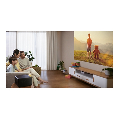 Familie schaut Film auf Leinwand, Projektor steht davor. Kind, Eltern sitzen auf Couch, lÃ¤cheln.