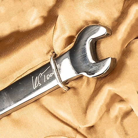 Nahaufnahme eines glänzenden Schraubenschlüssels auf beigem Stoff. Auf dem Werkzeug ist "US Tools 100" eingraviert.