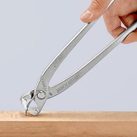 Tang trekt een spijker uit hout, vastgehouden door een hand.