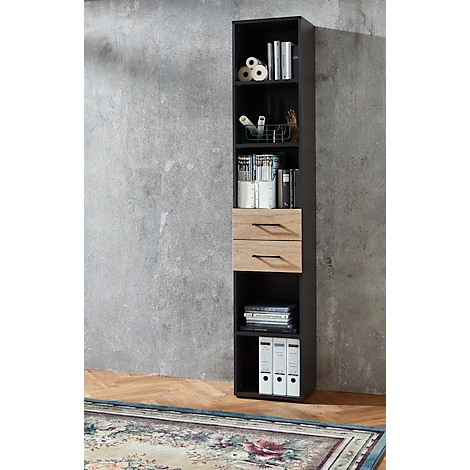 Étagère noire haute avec compartiments ouverts, tiroirs et éléments décoratifs, devant un mur gris.