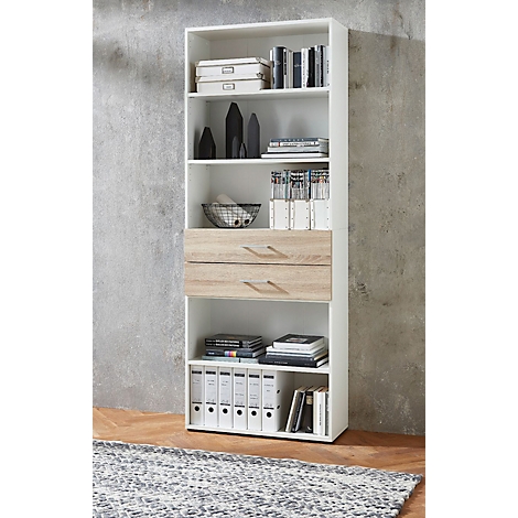 Bibliothèque blanche avec tiroirs, remplie de livres, de dossiers et d'objets de décoration. Devant un fond gris.