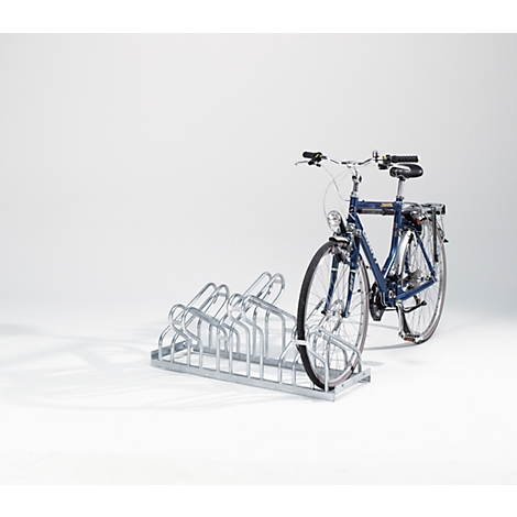 A blue bicycle stands in a metal bicycle rack against a white background.