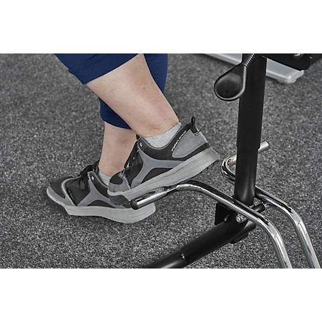 Close-up of feet in gray athletic shoes resting on a footrest of a black chair. The background is a gray carpet.