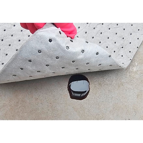Pink gloved hand lifting grey oil absorbent mat with black dots. Dark liquid visible underneath on a light surface.
