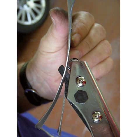 Nahaufnahme einer Hand, die mit einer Lochzange Metall formt. Im Hintergrund ist ein Reifen zu sehen.