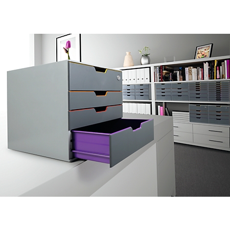 Meuble de bureau gris avec trois tiroirs. Le tiroir inférieur est partiellement sorti et de couleur violette.