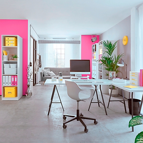 Espace de bureau lumineux avec des murs roses, un bureau, une chaise, des étagères et un canapé.
