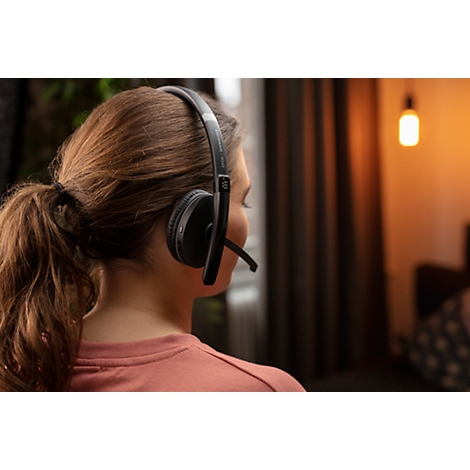 Woman wearing headphones with microphone, looking to the side. Lamp in the background.