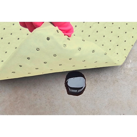 Une main gantée de rose soulève un chiffon jaune à pois foncés, révélant un liquide foncé sur une surface claire.