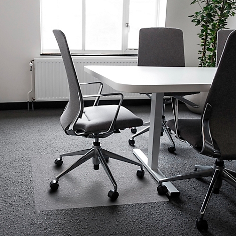 Bürostuhl mit Rollen vor weißem Tisch. Grau gemusterter Teppich, Fenster im Hintergrund.
