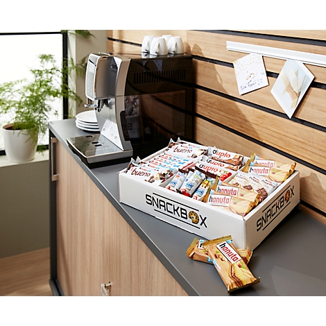 Une boîte à collations blanche avec divers bonbons est posée sur un comptoir à côté d'une machine à café. Derrière, un mur en bois.