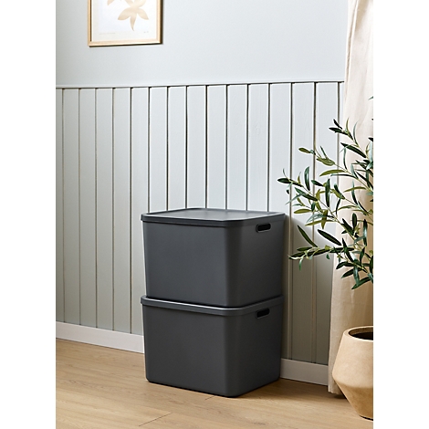 Deux boîtes de rangement grises sont empilées l'une sur l'autre, devant un mur lambrissé de panneaux verticaux.