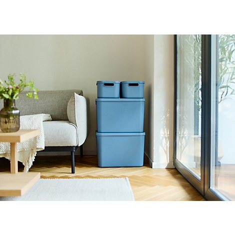 Boîtes de rangement bleu clair dans un salon. À côté, un canapé et une fenêtre avec vue sur la verdure.