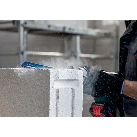 Eine Säge schneidet einen Gasbetonblock, Staubwolke entsteht.