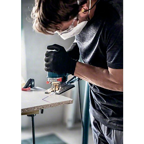 Ein Mann mit Schutzbrille, Maske und Handschuhen sägt mit einer Stichsäge Holz. Auf dem Holz ist eine Linie eingezeichnet.