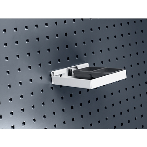 Graue Lochwand mit einem weißen Regal, das eine schwarze, unterteilte Ablage hält.