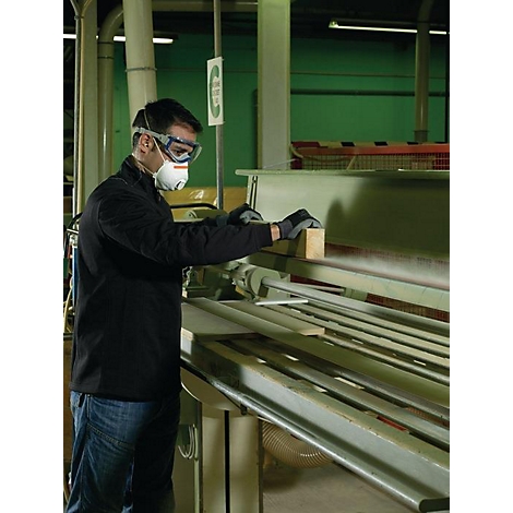 Un homme portant des lunettes de protection et un masque travaille le bois sur une machine dans un atelier.