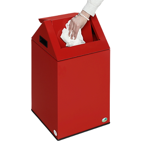 A hand is throwing a white cloth into a red trash can. The bin has a slanted top.