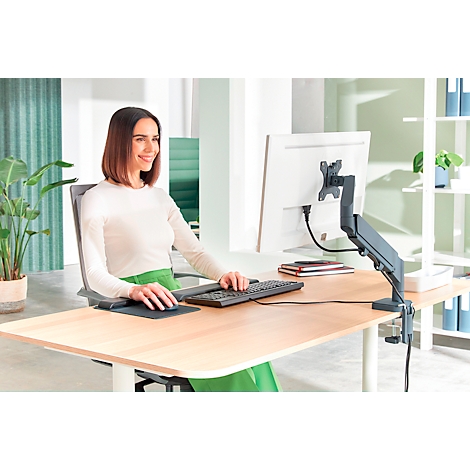 Une femme est assise à un bureau et travaille sur l'ordinateur. Elle sourit en utilisant le clavier et la souris.
