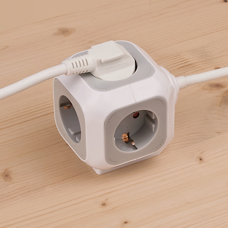 Cube blanc et gris avec 3 prises, une prise est insérée. Posé sur une surface en bois.
