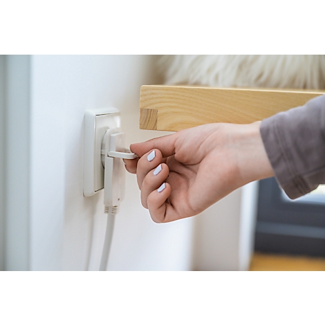 Une main retire une prise de la prise de courant. La main a les ongles vernis. La prise est sur un mur blanc.