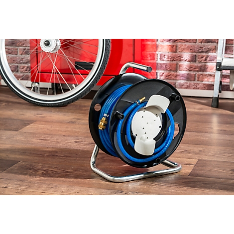 A blue garden hose reel with a metallic frame. In the background, a bicycle and a brick wall are visible.